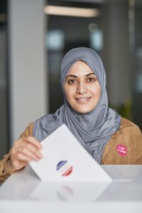 Smiling woman in hijab casting her vote during election day indoors.