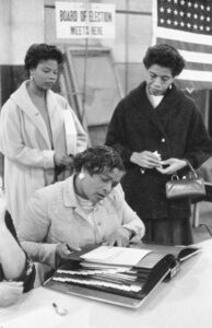 Three African American women at a polling place, one looking at a book of registered voters on November 5, 1957, in New York City or Newark, New Jersey.